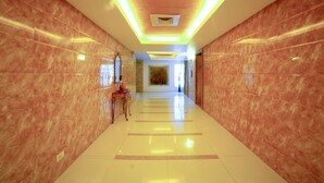 A long, well-lit hallway with marble walls and a shiny floor, leading to a room with a large painting and a window.