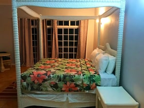 Een hemelbed met een bloemenbedekking, een nachtkastje en gordijnen.