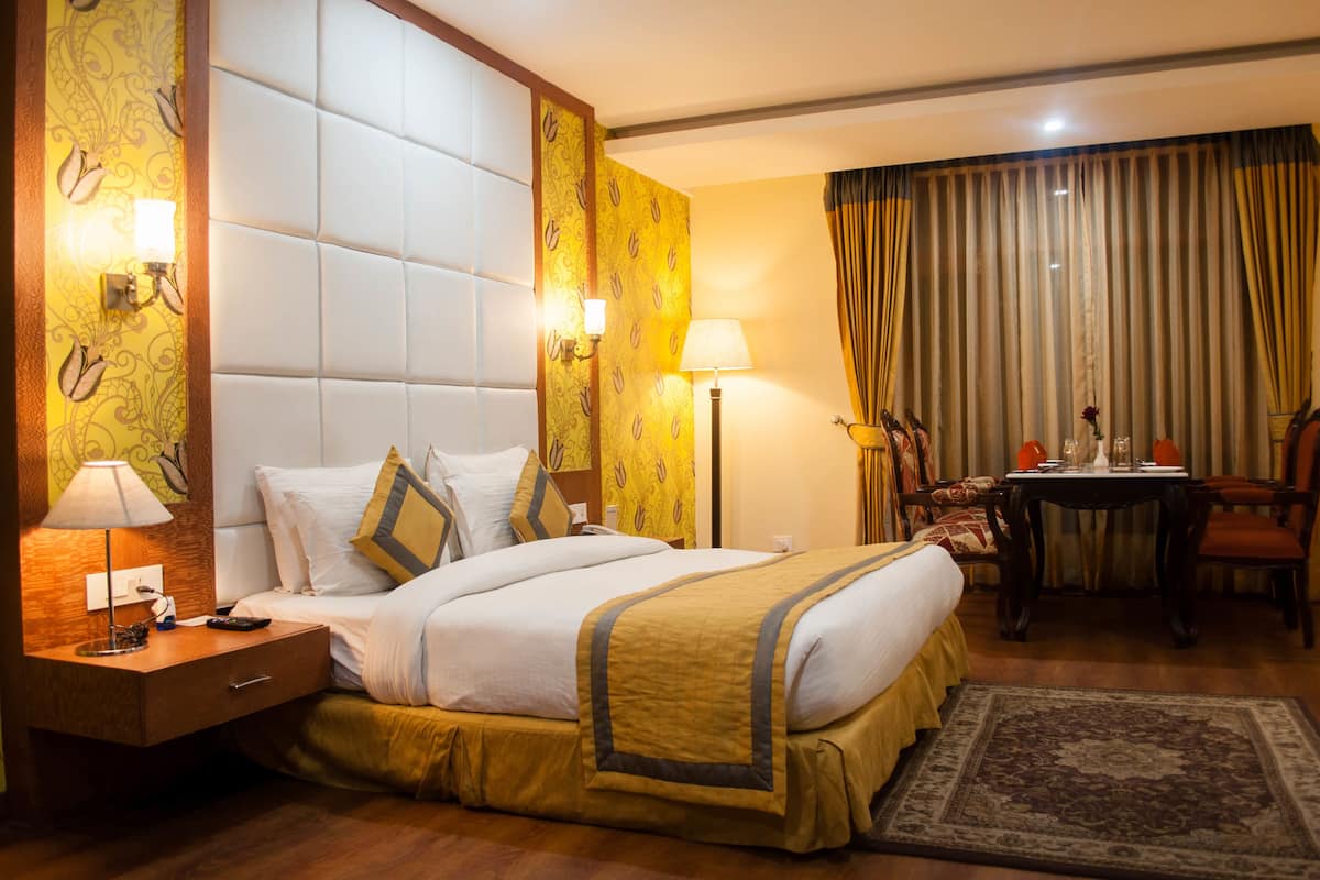 Quarto de hotel com uma cama grande, uma mesa de cabeceira com abajur, uma mesinha com um vaso e uma cadeira.