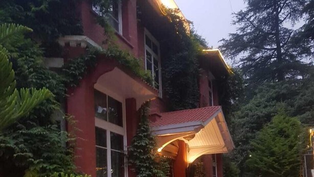A red building with a covered entrance, surrounded by potted plants and a red pathway leading to the entrance. - Hotel Southgate Shimla (Shimla)