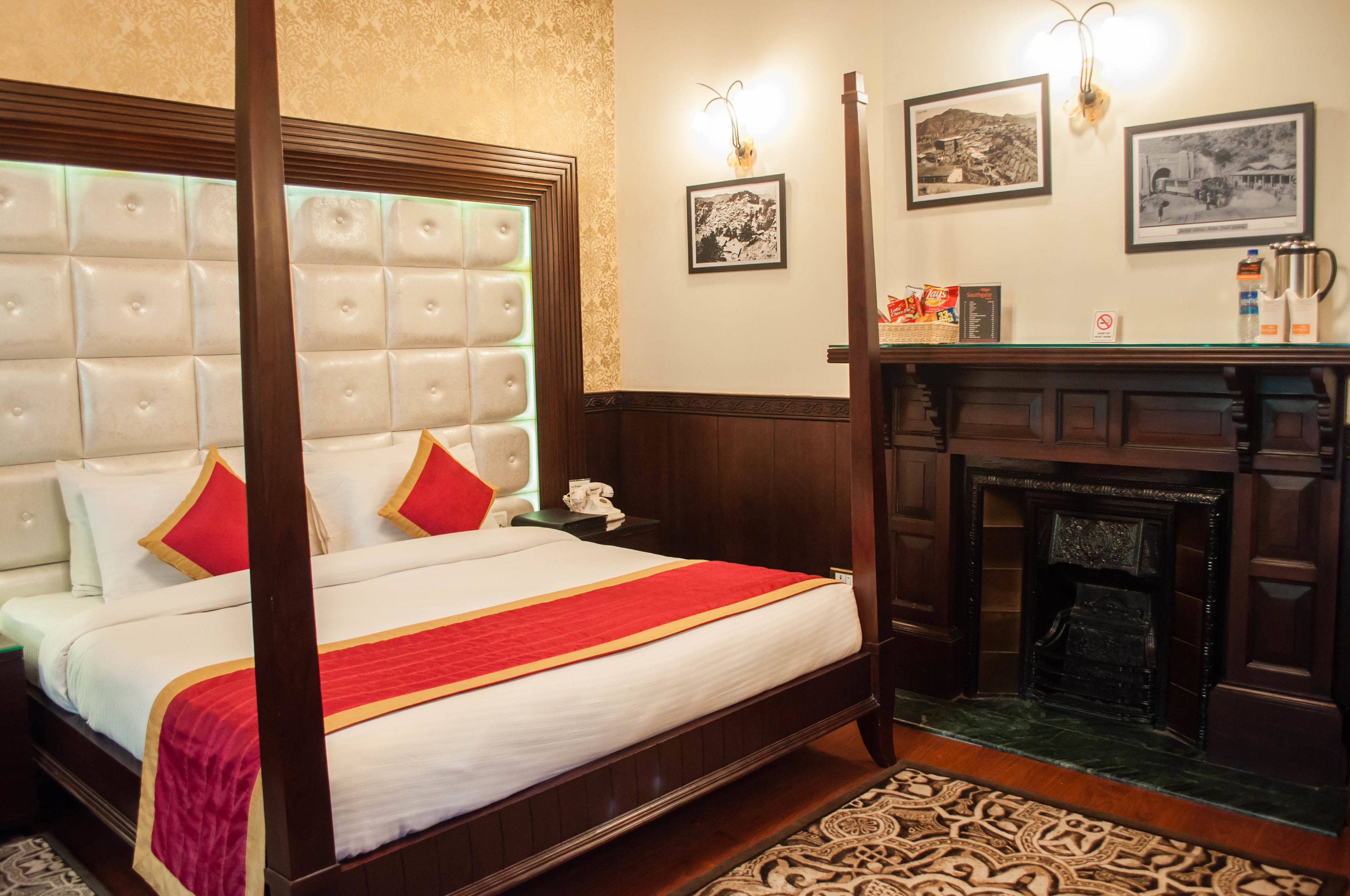 Una cama con dosel con un edredón rojo y blanco, un cabecero de madera y una mesita de noche con un teléfono.