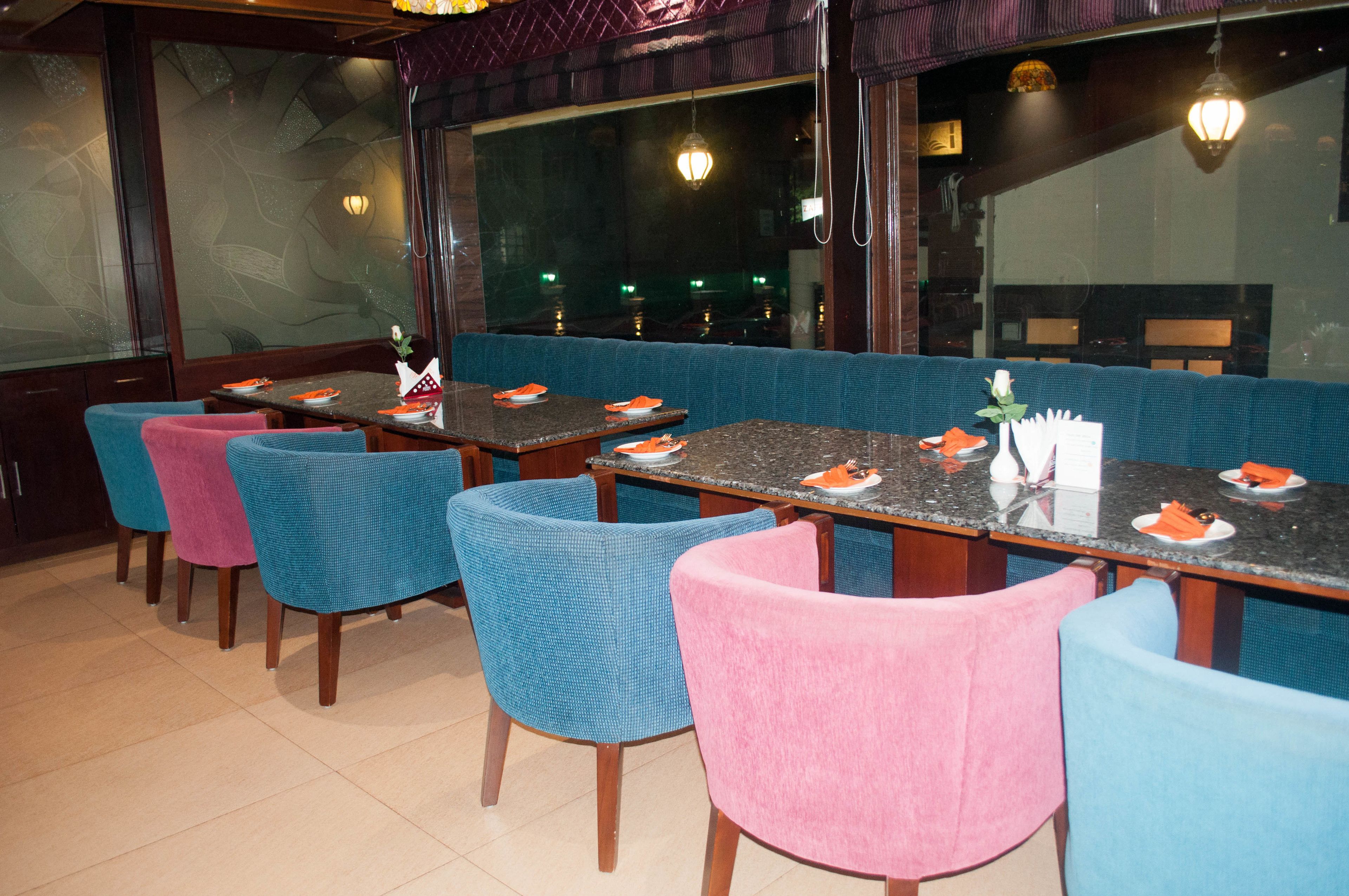 A restaurant with blue and pink chairs, wooden tables, and a view through large windows.