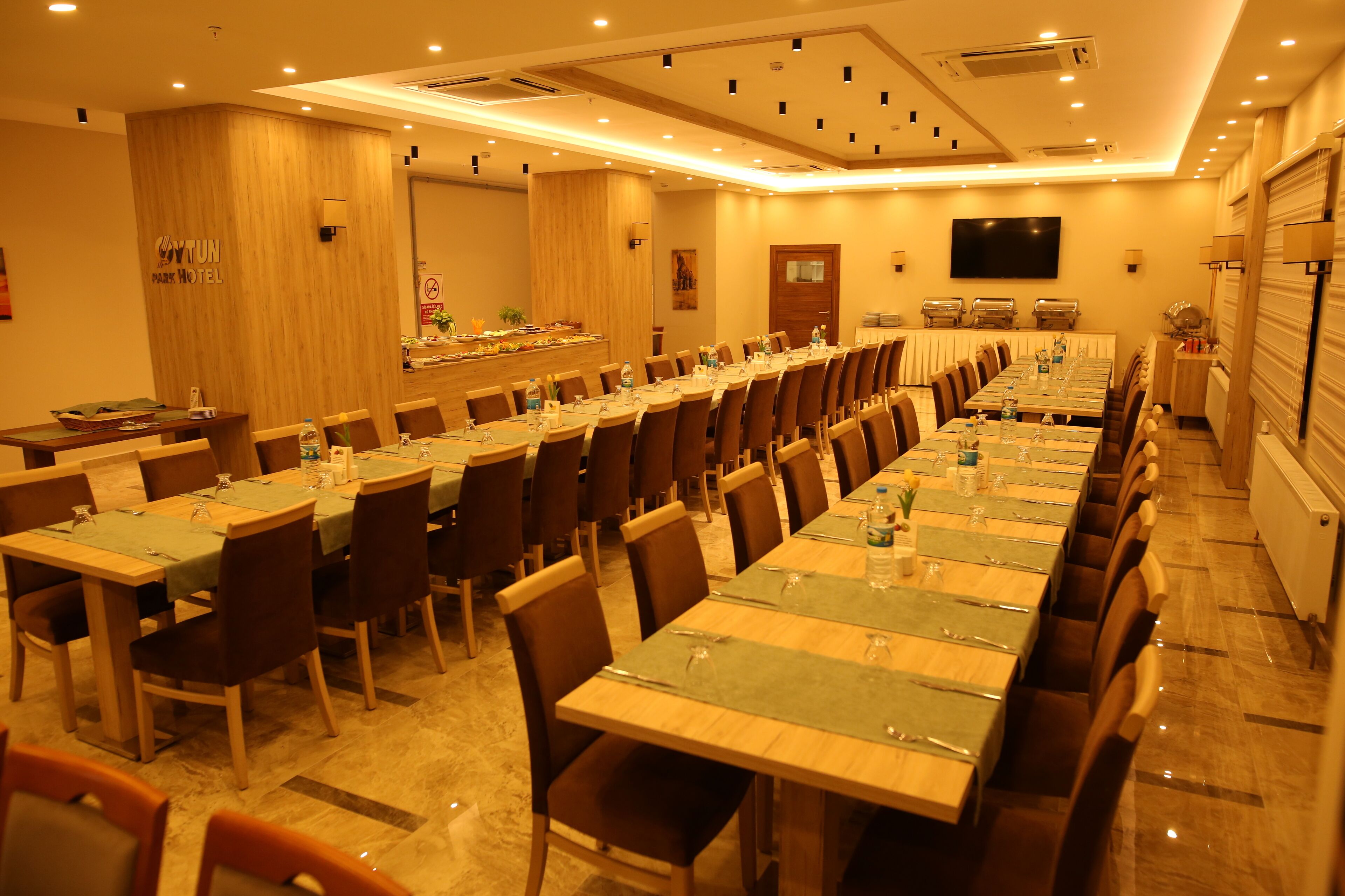 A conference room with multiple tables and chairs, a TV screen, and a buffet area.