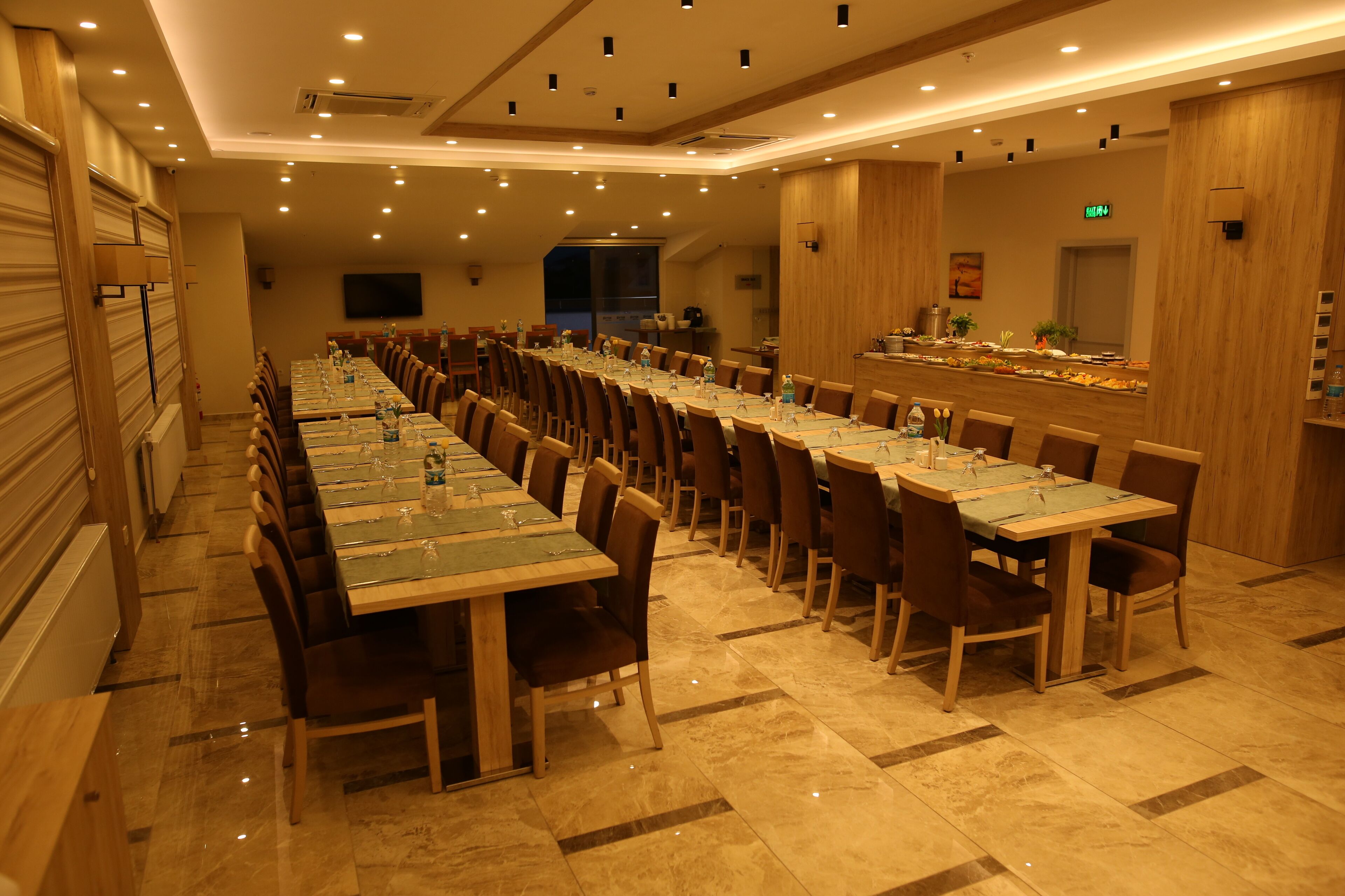 Una larga mesa de comedor con sillas, una zona de buffet y una pantalla de televisión en la pared.