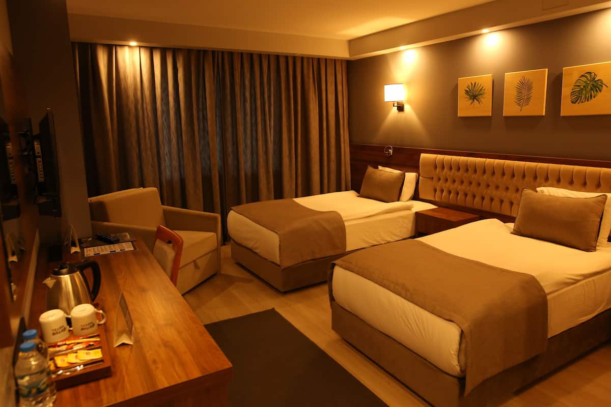 A hotel room with two beds, a desk with a coffee maker, a chair, and a TV.