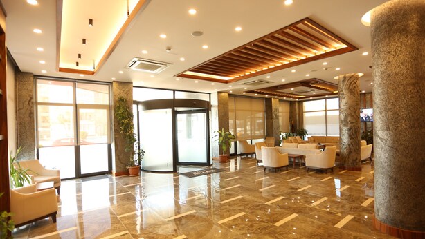A lobby with a marble floor, a reception desk, seating area, and a large pillar. - Oytun Park Hotel (Çanakkale)