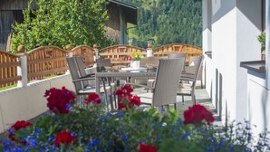 A terrace with wicker furniture, a glass table, and red flowers. - Tobhartbauer (Dorfgastein)
