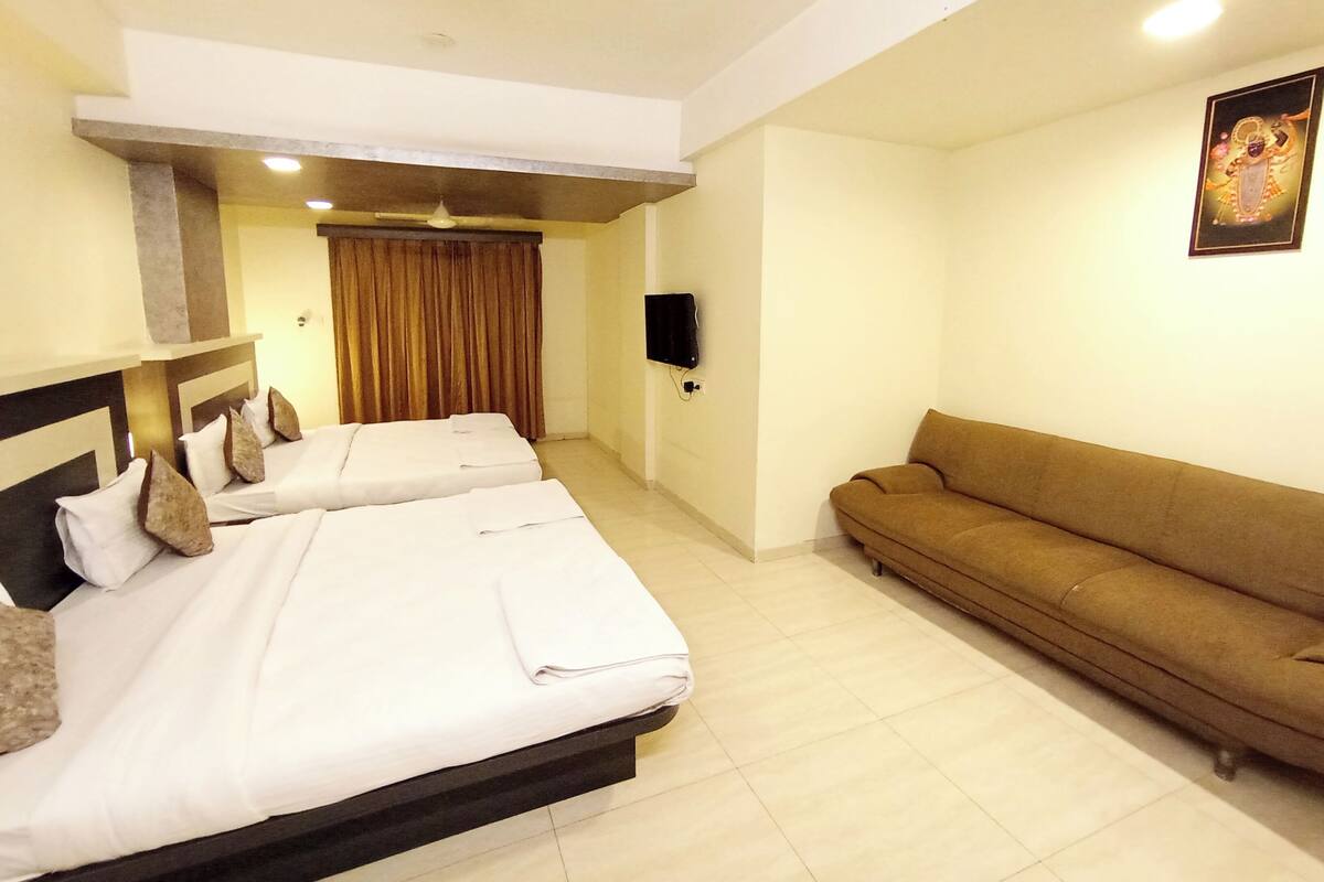 Habitación de hotel con dos camas, un sofá, un televisor de pantalla plana y un ventilador de techo.