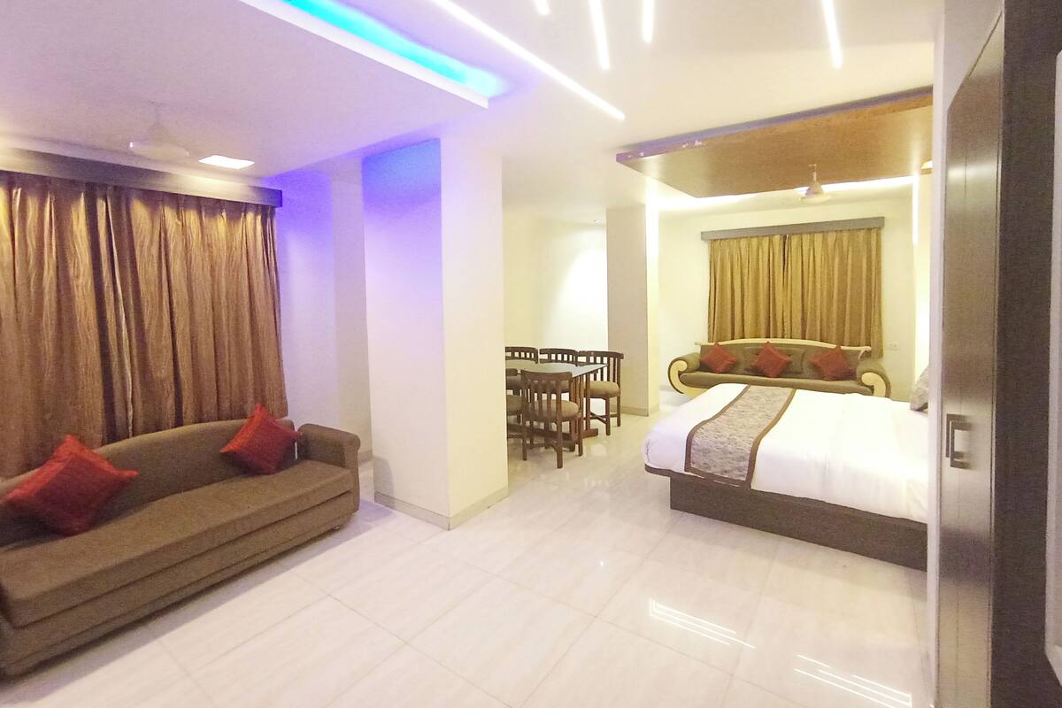Habitación de hotel con cama, sofá, mesa de comedor con sillas y una zona de comedor separada.