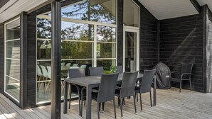 Un espace extérieur aménagé pour les repas, avec une table et des chaises, de grandes fenêtres et une terrasse en bois.