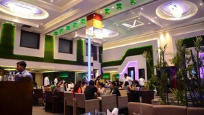 A spacious indoor dining area with high ceilings, modern lighting fixtures, and green accent walls. - The Vivaan Hotel & Resorts (Nilokheri)
