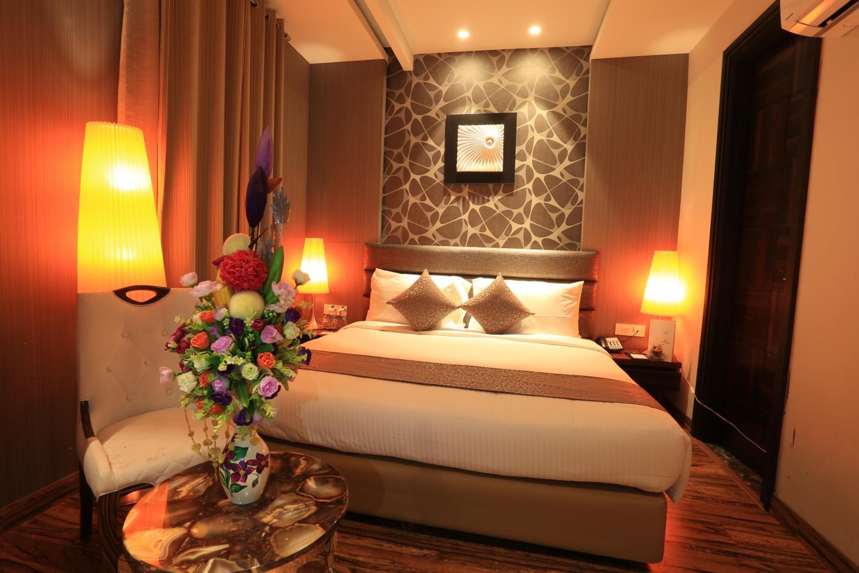 A hotel room with a large bed, two bedside lamps, a vase of flowers, and a small round table with a glass.