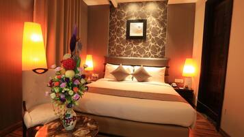 A hotel room with a large bed, two bedside lamps, a vase of flowers, and a small round table with a glass.