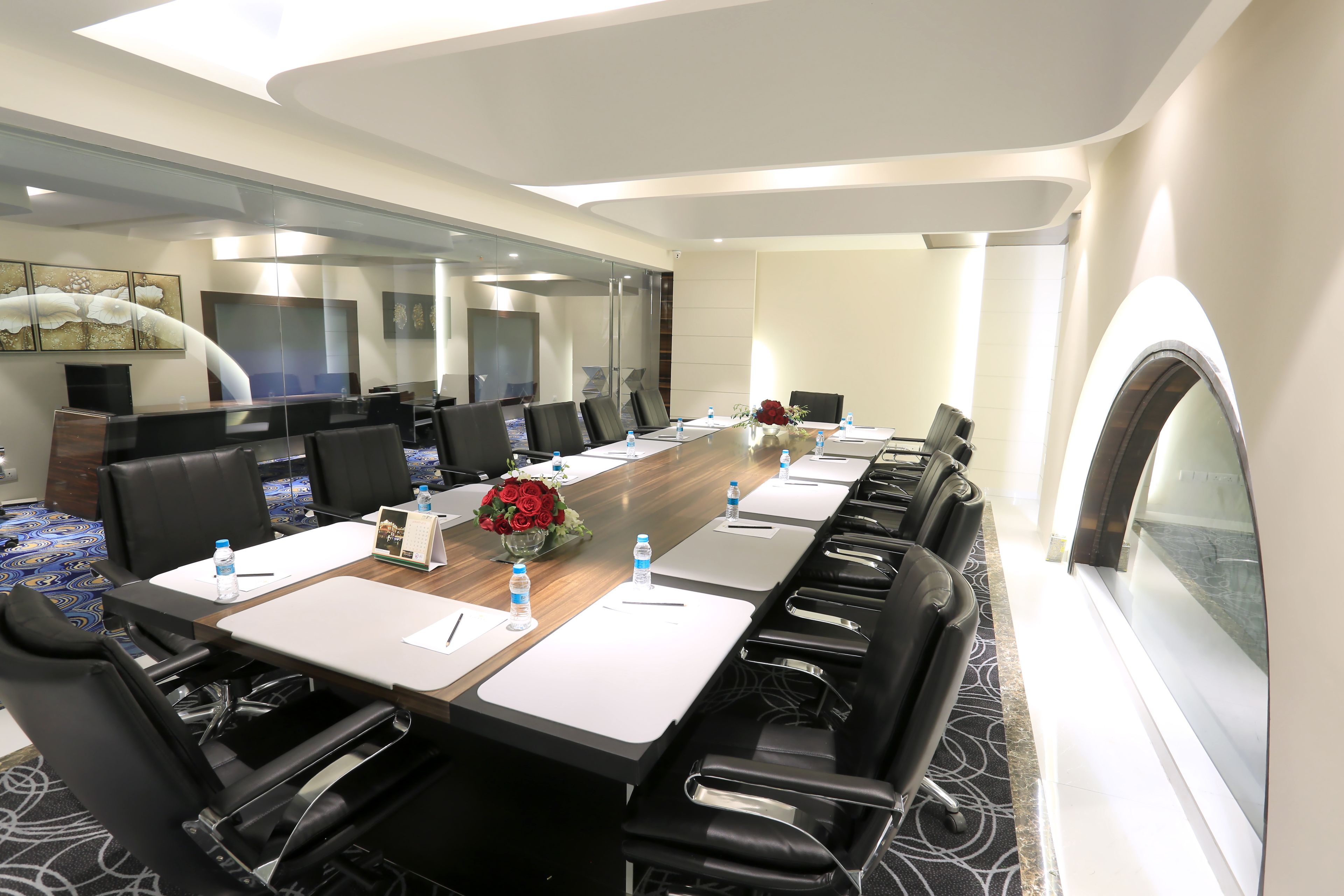A conference room with a long table, black chairs, water bottles, and a vase of flowers.