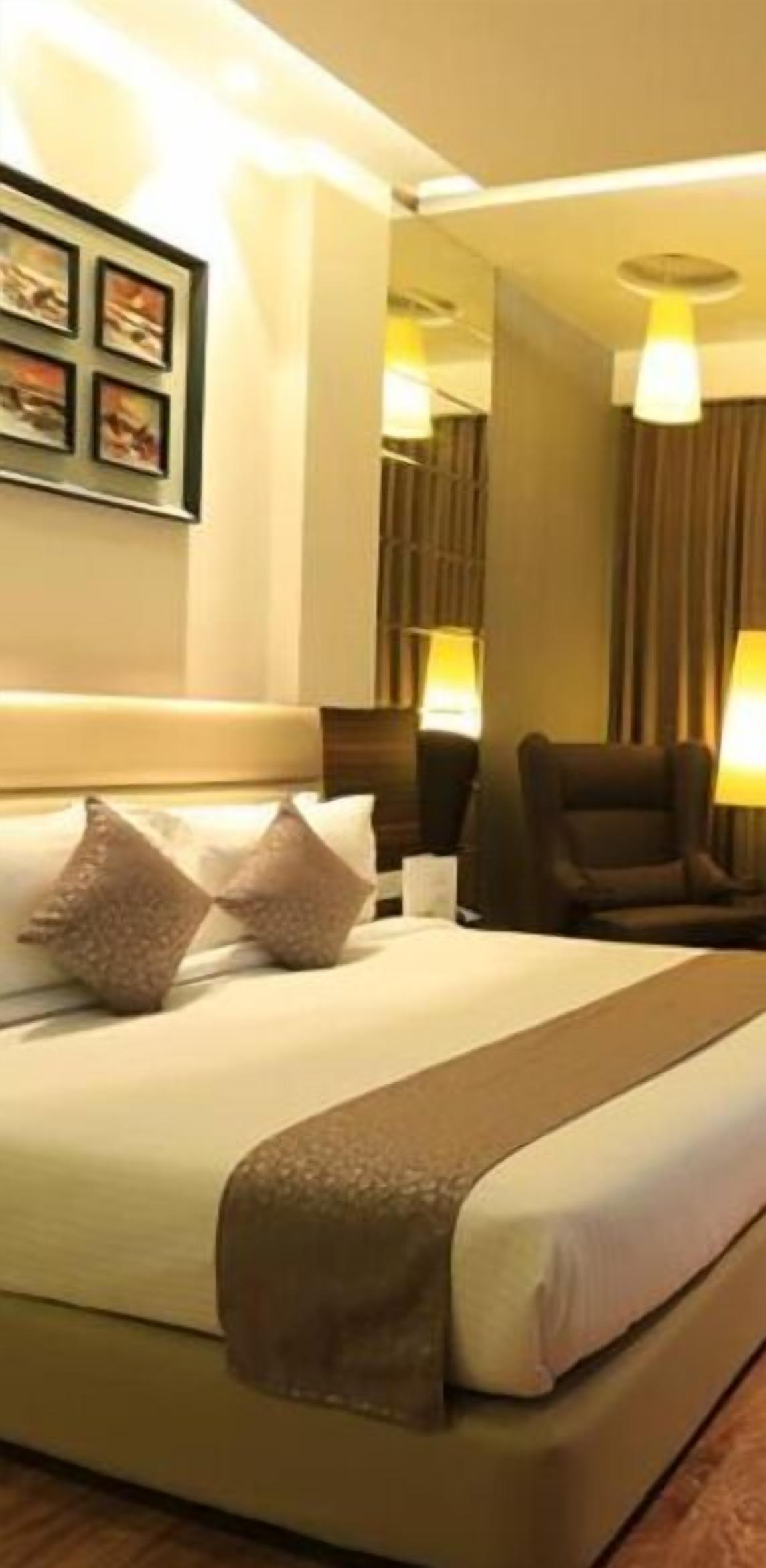 A hotel room with a large bed, a headboard, a desk, two chairs, and a lamp.