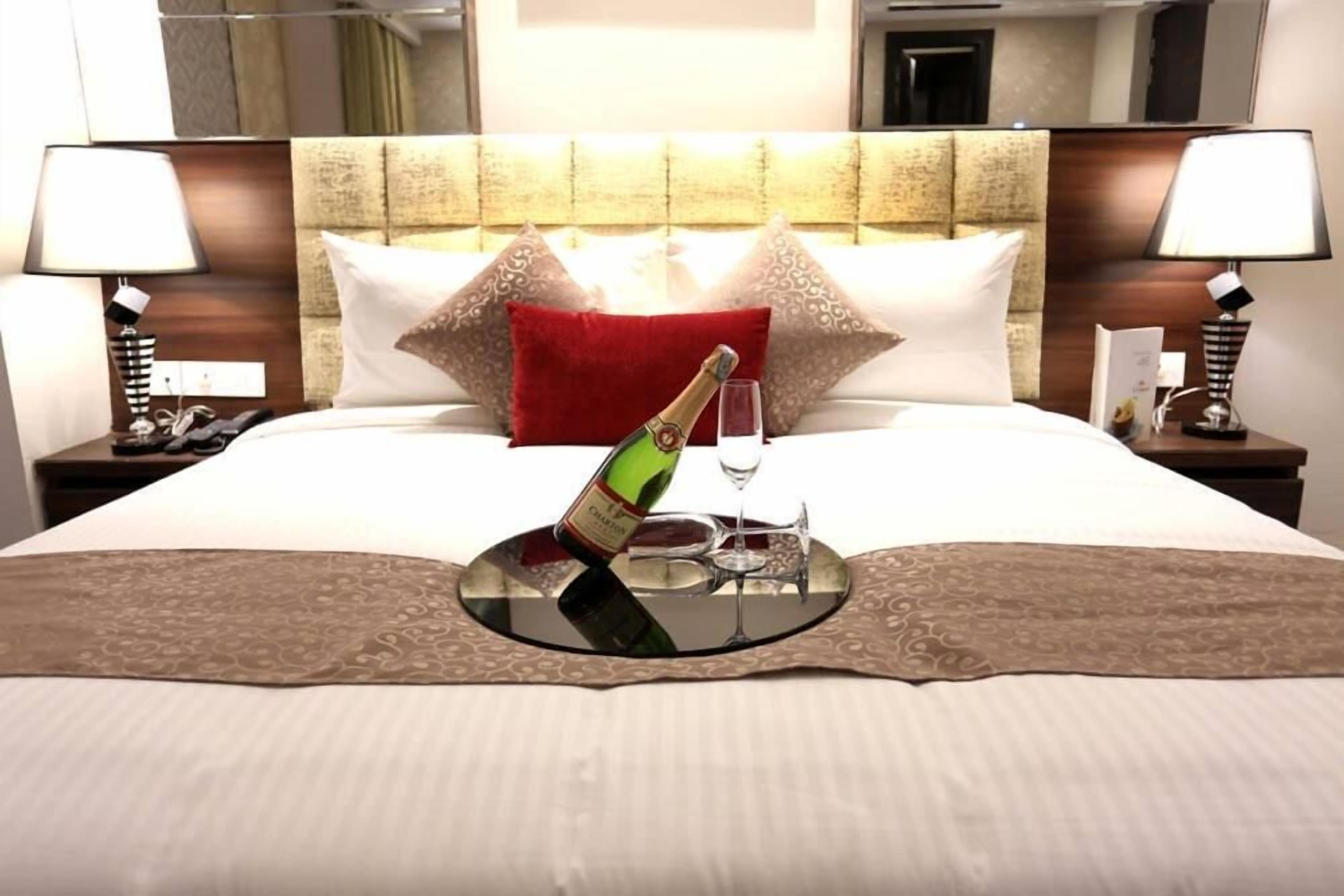 A hotel room with a neatly made bed, a bedside table with a lamp, and a nightstand with a phone.