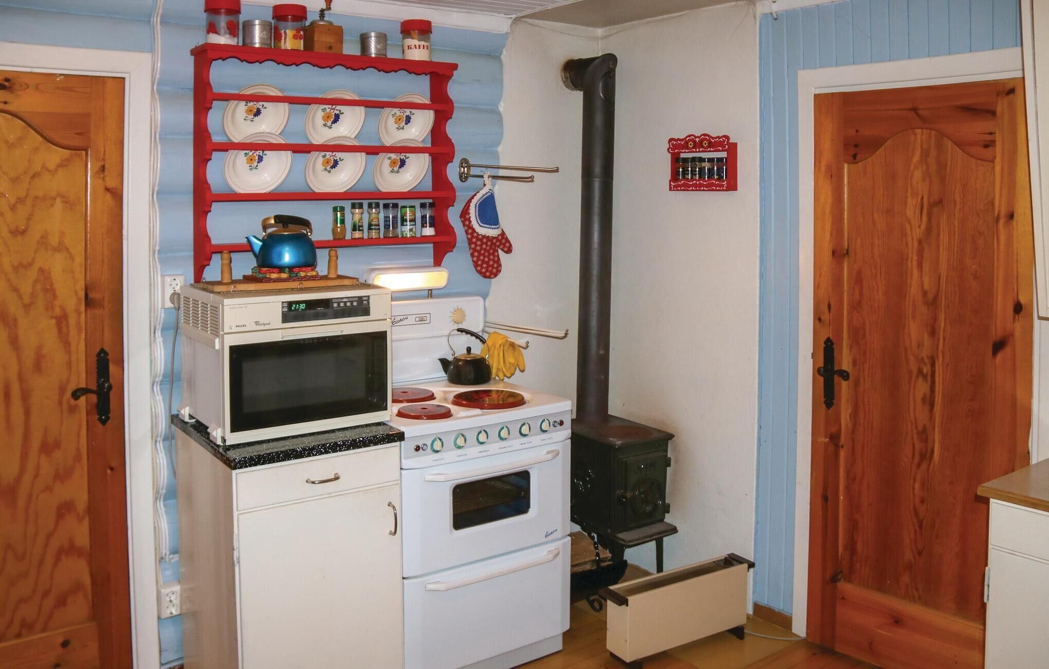 A compact kitchen with a white stove, oven, and microwave, a red shelf with plates, and a black chimney.