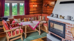 A cozy cabin interior with a wooden bench, a table with a pink tablecloth, a fireplace, and a scenic view through the windows. - 3 bedroom stunning home in Sjusjøen (Sjusjøen)
