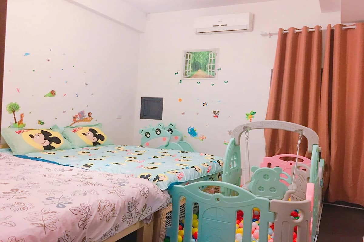 Un dormitorio infantil con dos camas, un corralito y adornos en la pared.