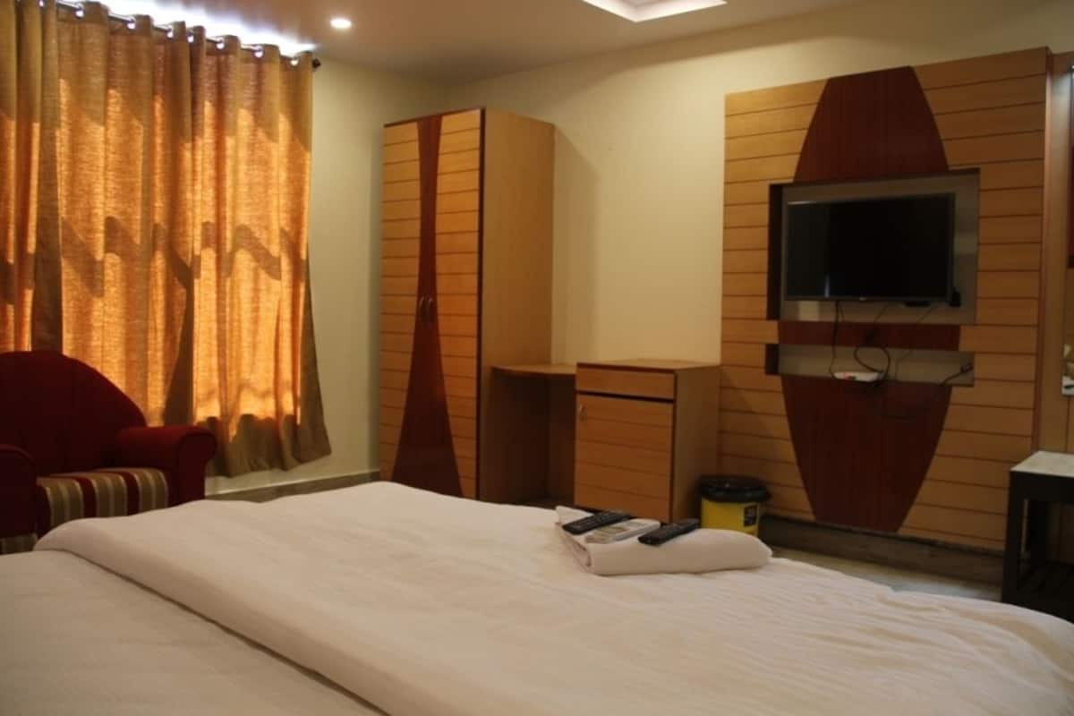 A hotel room with a large bed, a TV mounted on the wall, a wardrobe, and a desk.