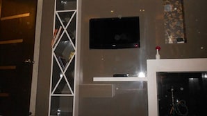 Una sala de estar con un televisor montado en la pared, una estantería blanca y una chimenea.