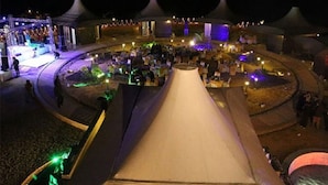 Evento nocturno al aire libre con carpas y un escenario, rodeado de gente.
