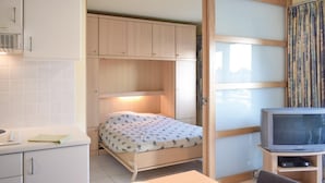 Una camera compatta con un letto, una piccola televisione e un angolo cottura.