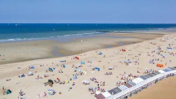 Una spiaggia con numerosi lettini e ombrelloni, un molo che si protende sull'acqua, e un cielo sereno.