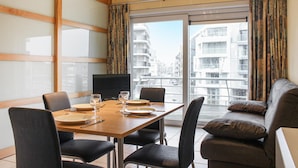 Una camera d'albergo con un tavolo da pranzo apparecchiato per quattro persone, un divano e un'ampia finestra che si affaccia su edifici.