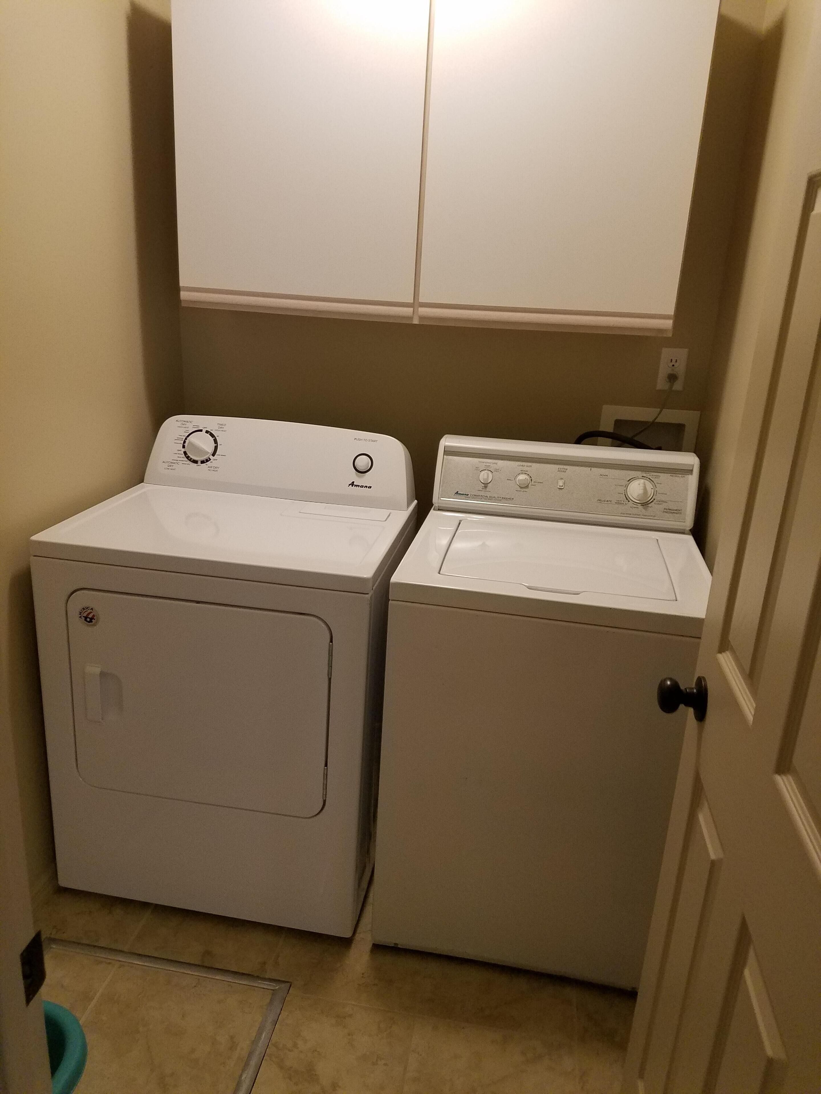 A laundry room with two stacked washers and dryers, a door, and a light switch on the wall.