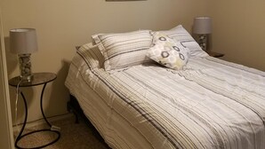 Ein Schlafzimmer mit einem Bett, zwei Nachttischlampen, einem Blumenbild an der Wand und einem Teppichboden.