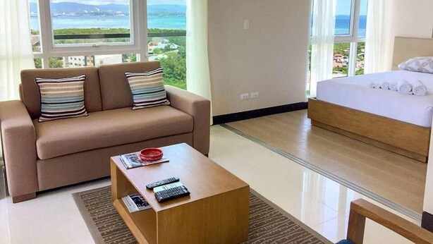 A modern hotel room with a sofa, a coffee table, and a bed. - Condo Apartment in Mactan Newtown (Lapu-Lapu)