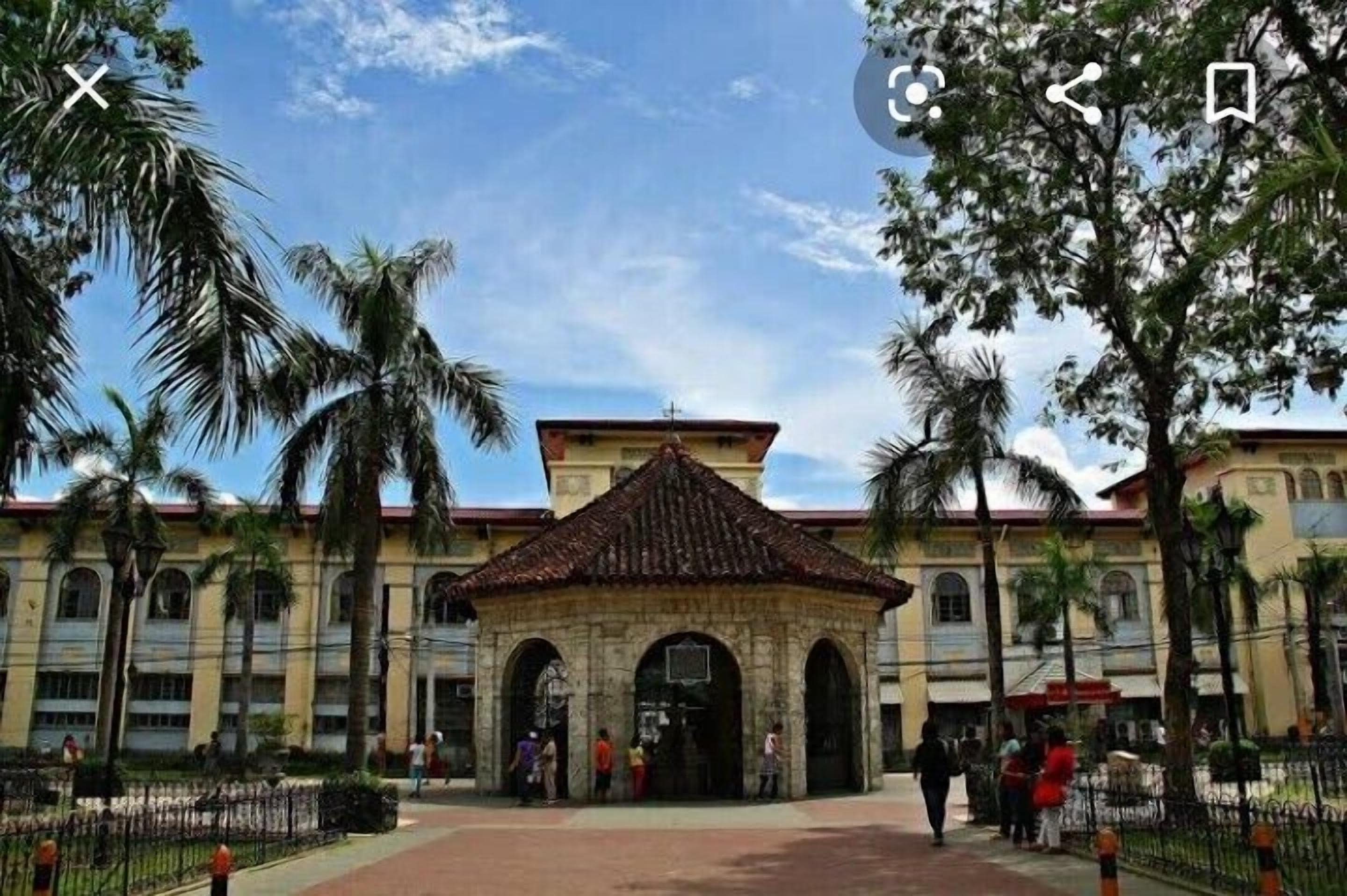 A colonial-style building with a central courtyard, palm trees, and a clear sky.