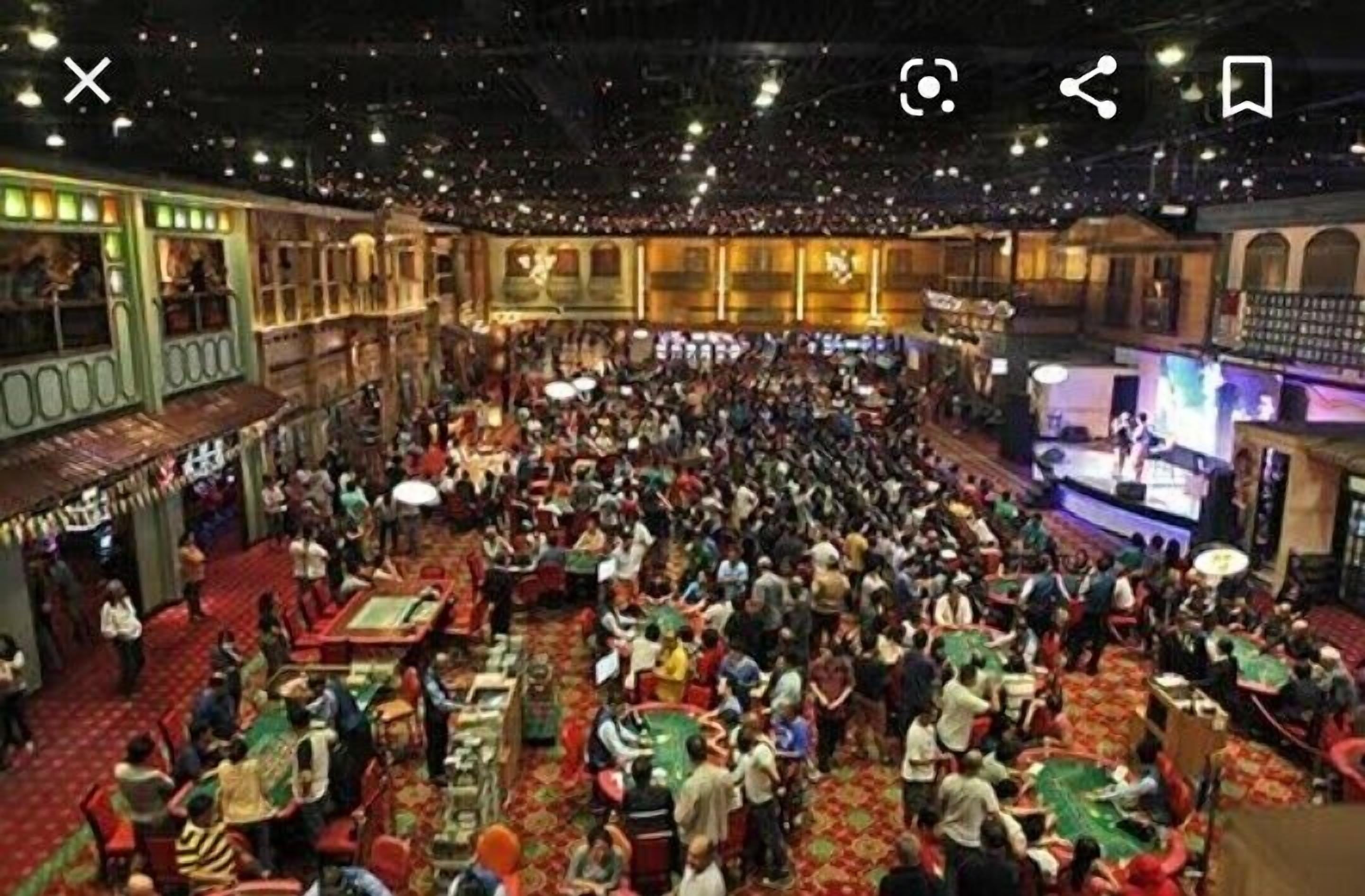 A crowded casino with multiple gaming tables and a stage.