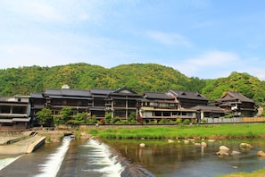 A traditional Japanese ryokan with a river flowing through it, surrounded by lush greenery and hills. - Ryokan Ohashi (Misasa)
