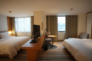 Ein Hotelzimmer mit zwei Betten, einem Schreibtisch mit Computer, einem Stuhl und Blick auf die Stadt.