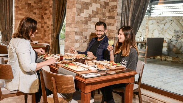 A group of people dining at a table with a brick wall and curtains in the background. - Sarajevo Suit Hotel (Cayirova)