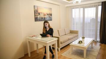 A modern living room with a sofa, a glass coffee table, and a white table. A painting is on the wall, and a laptop is on the table.
