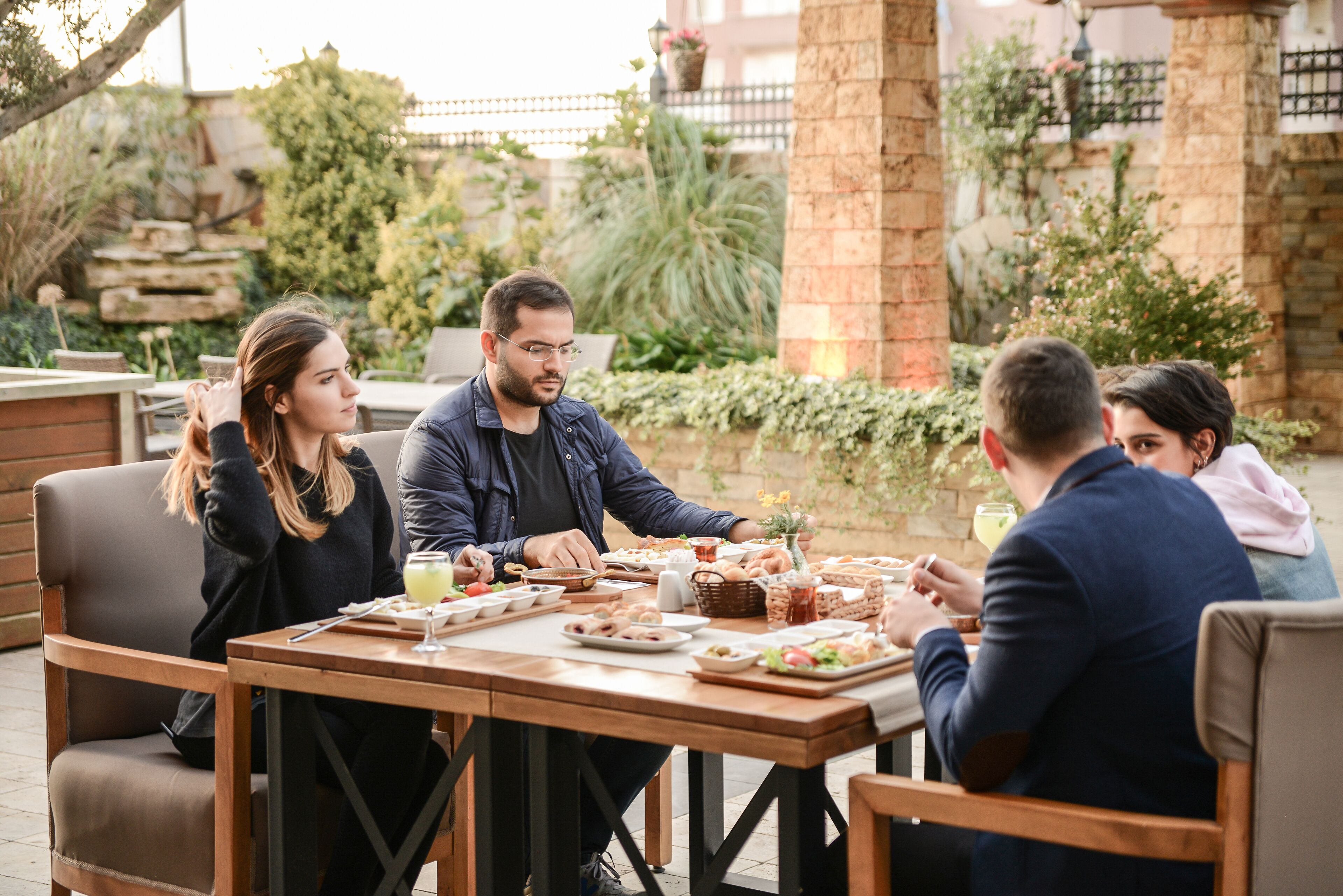 Un grup de persones dinant a una taula a l'aire lliure, amb diversos plats i begudes.