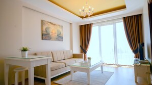 A modern living room with a sofa, glass coffee table, and a small table with a plant. - Sarajevo Suit Hotel (Cayirova)