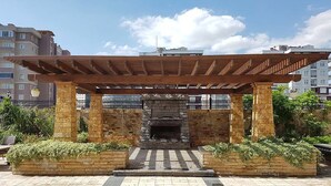 A covered outdoor area with a stone fireplace, surrounded by planters and a tiled floor. - Sarajevo Suit Hotel (Cayirova)