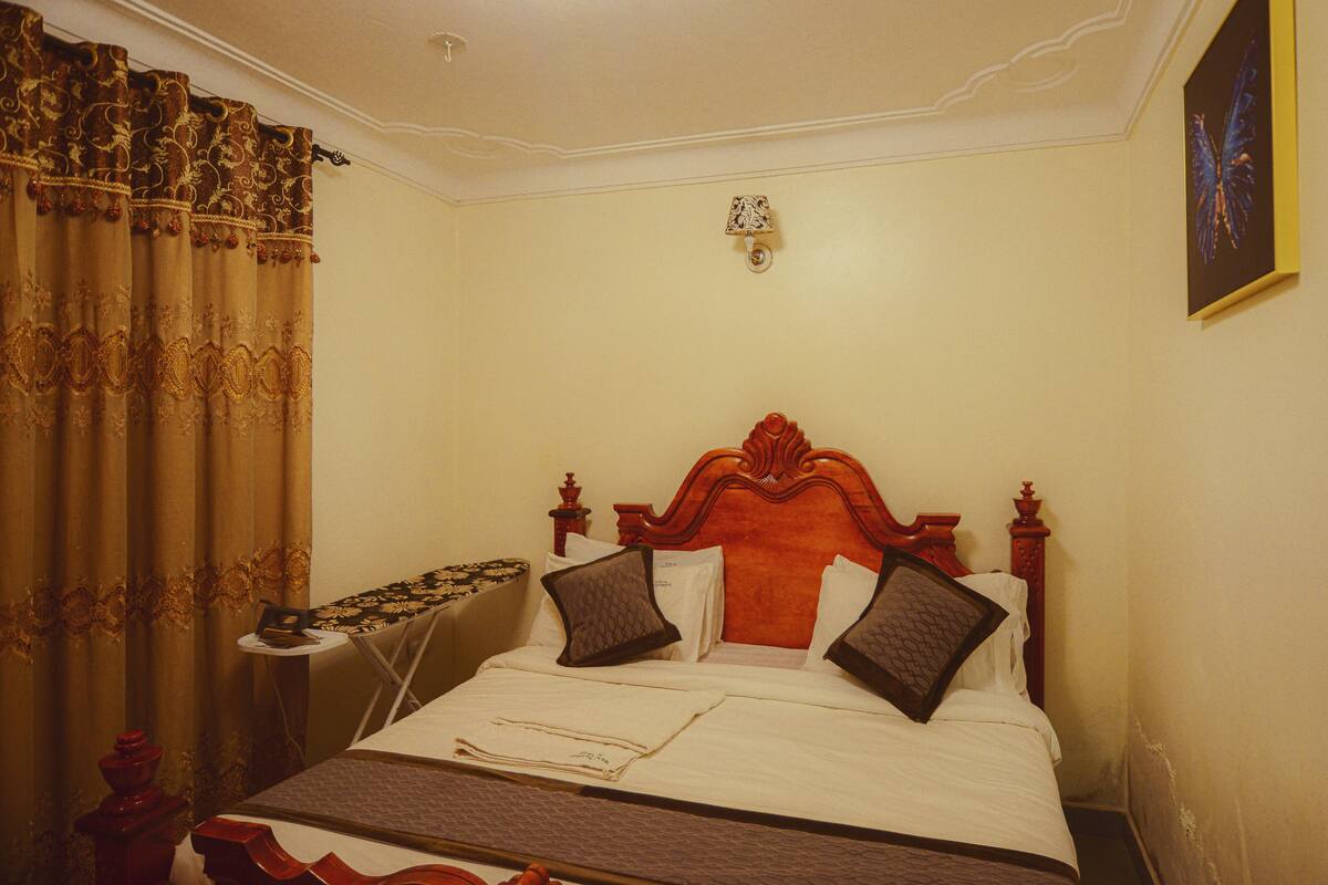 A neatly made bed with a wooden headboard, a bedside table with a lamp, and a decorative curtain.