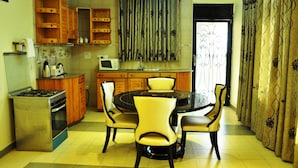 A compact kitchen with a dining area, featuring a stove, microwave, and wooden cabinets. - Evelyn Apartments (Kampala)