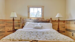 A wooden bed with a patterned bedspread, two bedside lamps, and a window with a view of trees. - 'Hiawatha' Peaceful Living in Rocky Mtn Nat'l Park (Allenspark)