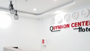 A reception desk with a wooden top and grey base, two black office chairs, and a wall clock with multiple time zones. - Khách sạn Quy Nhơn Center (Quy Nhon)