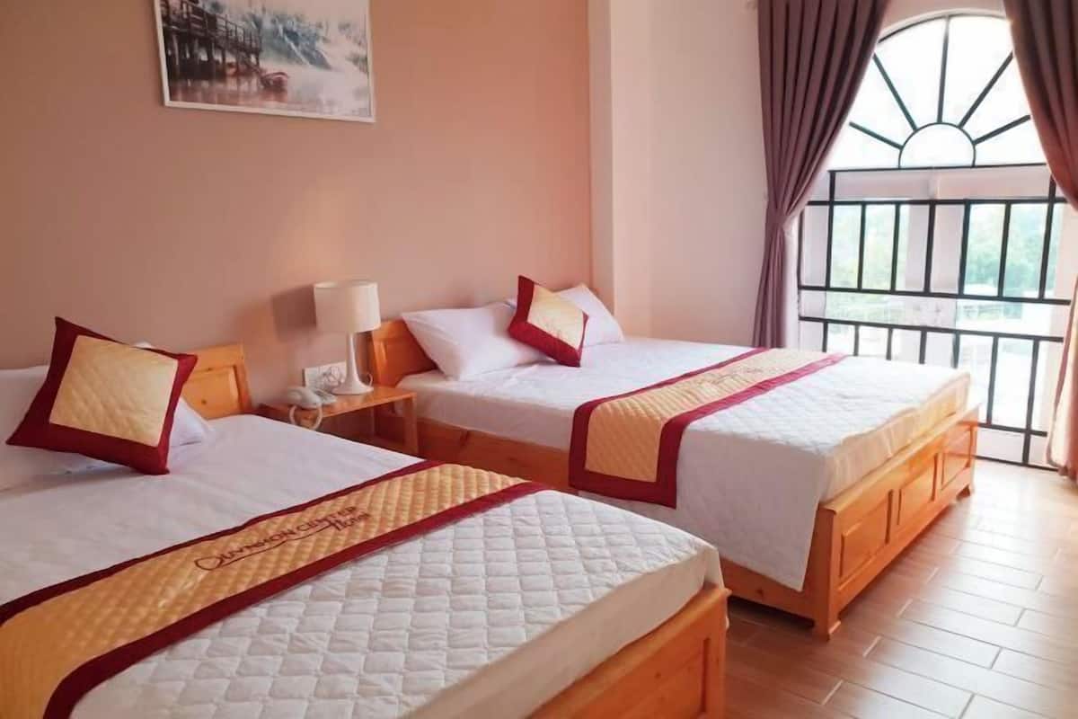 Two twin beds with matching headboards, a bedside table with a lamp, and a window with a view of greenery.