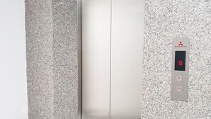 A modern elevator with a digital display, set in a room with a speckled granite wall and a small, metallic side table. - Khách sạn Quy Nhơn Center (Quy Nhon)