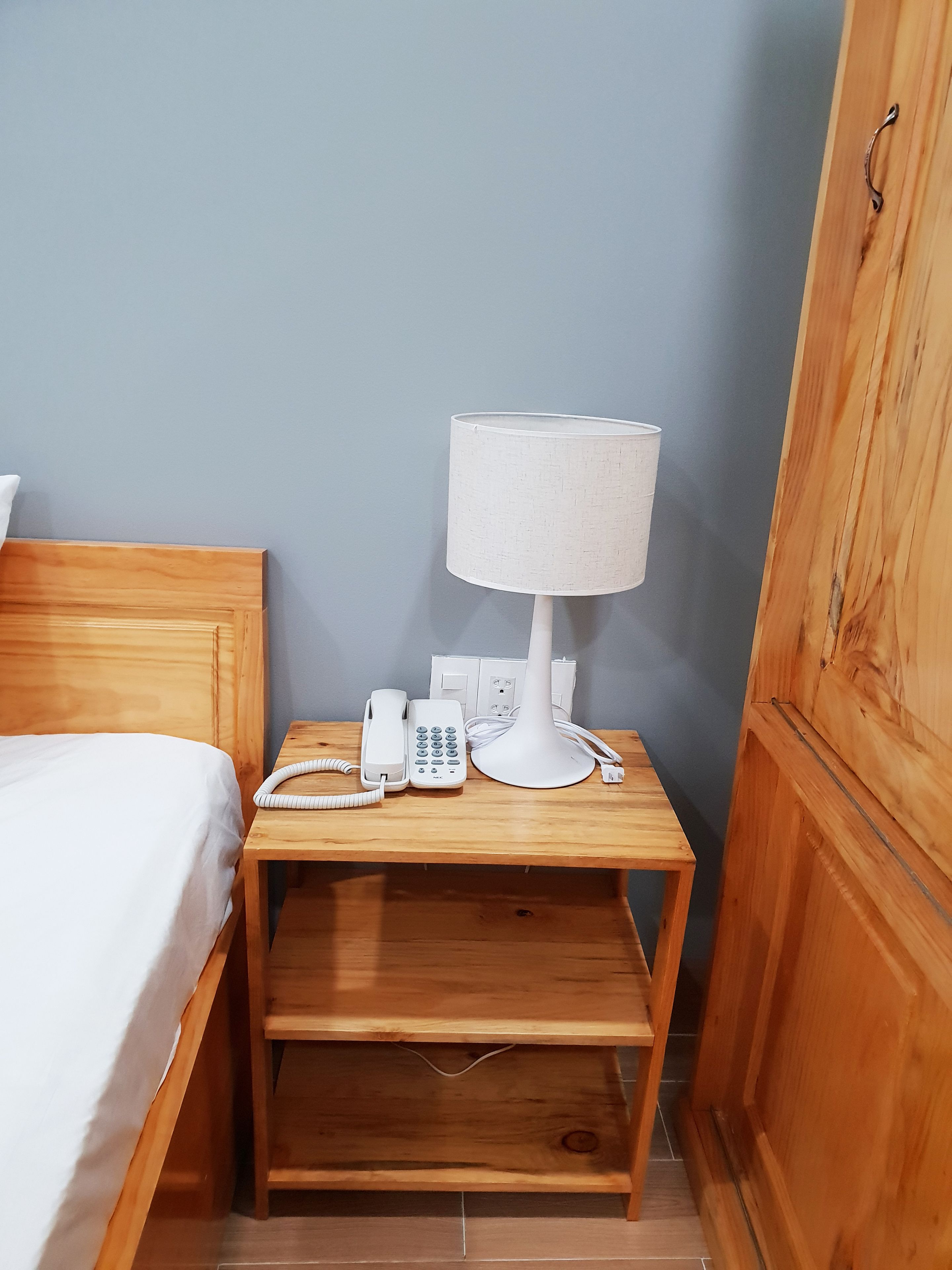 Ein Nachttisch aus Holz mit einer weißen Lampe, einem Telefon und einer Steckdose.