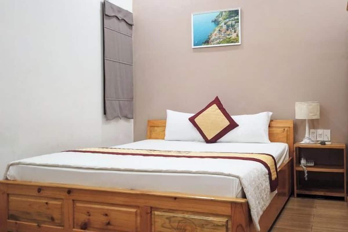 A bedroom with a wooden bed, a nightstand with a lamp, and a wall-mounted picture.