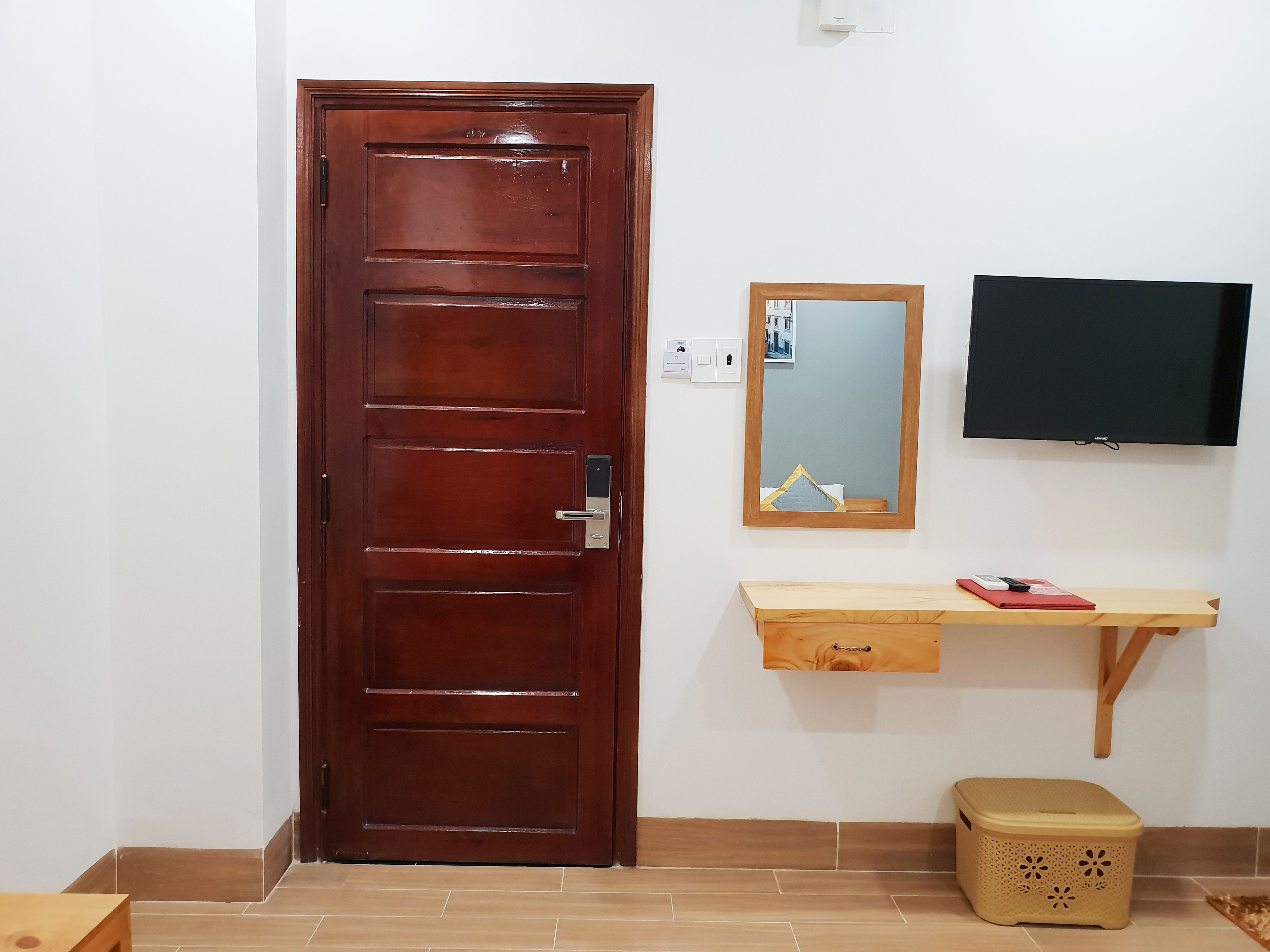 Une porte en bois avec une poignée, une petite étagère en bois avec un miroir, un téléviseur fixé au mur et une poubelle.